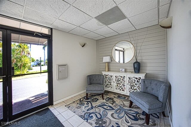 living area with a paneled ceiling, wooden walls, and light tile patterned flooring