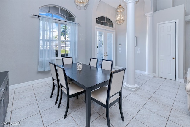 tiled dining room featuring a towering ceiling, decorative columns, a notable chandelier, and french doors