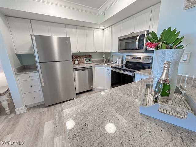 kitchen featuring light wood-type flooring, appliances with stainless steel finishes, light stone counters, white cabinetry, and ornamental molding