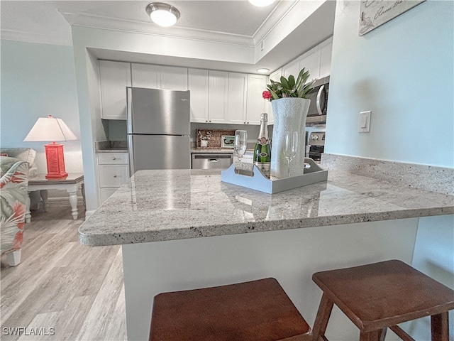 kitchen with light hardwood / wood-style flooring, stainless steel appliances, ornamental molding, kitchen peninsula, and white cabinets