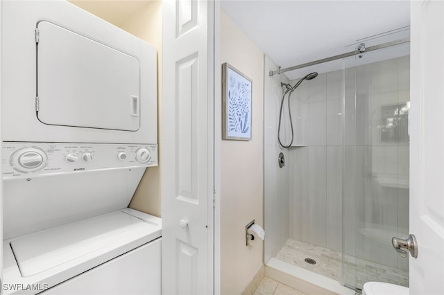 bathroom featuring a shower with door, stacked washer and clothes dryer, toilet, and tile patterned flooring