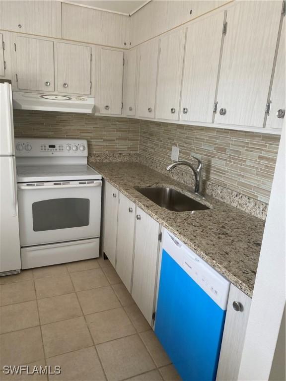 kitchen featuring light tile patterned floors, under cabinet range hood, white appliances, a sink, and decorative backsplash