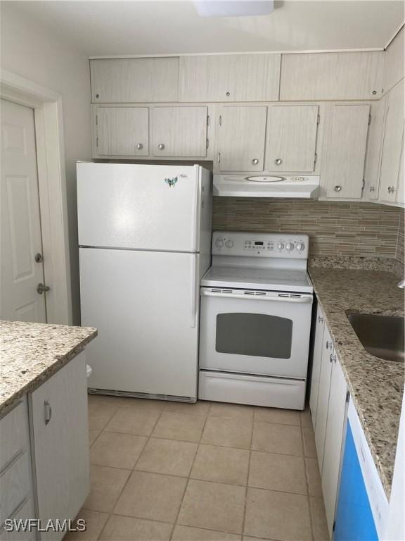 kitchen featuring light tile patterned flooring, under cabinet range hood, white appliances, a sink, and light stone countertops