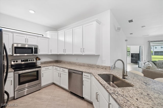 kitchen featuring light tile patterned floors, appliances with stainless steel finishes, sink, white cabinetry, and light stone counters