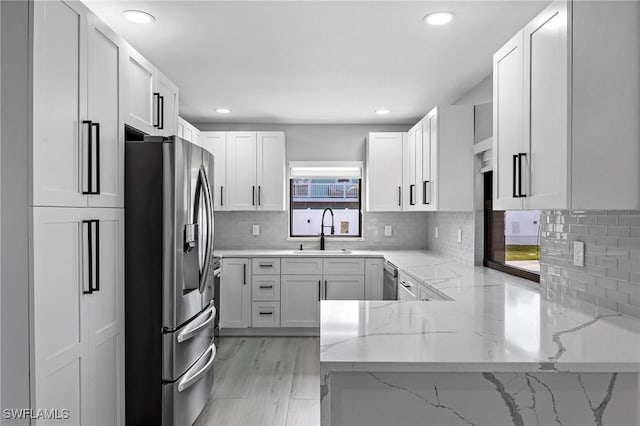 kitchen featuring white cabinets, light stone counters, stainless steel appliances, and a sink