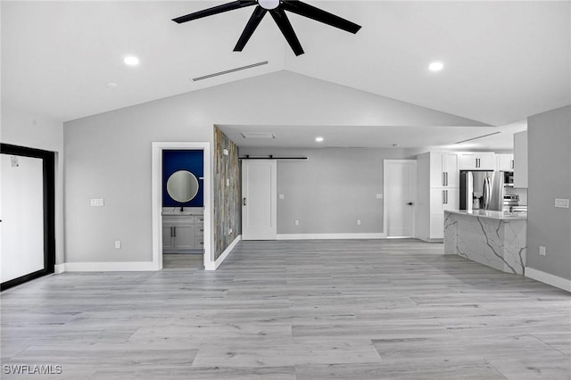 unfurnished living room featuring a barn door, visible vents, a ceiling fan, baseboards, and light wood-type flooring