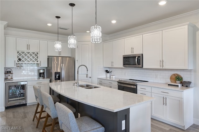 kitchen featuring a center island with sink, beverage cooler, appliances with stainless steel finishes, sink, and light wood-type flooring