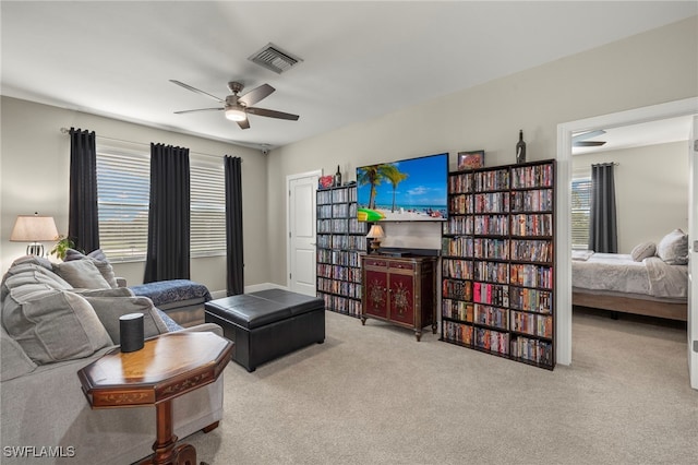 living area featuring a wealth of natural light, visible vents, a ceiling fan, and carpet