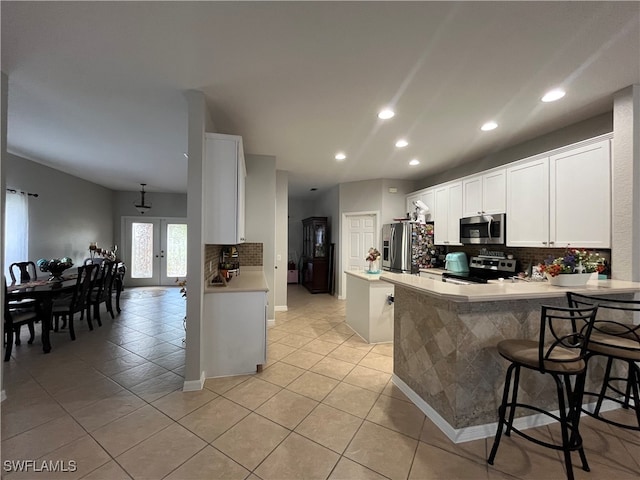 kitchen with appliances with stainless steel finishes, kitchen peninsula, a kitchen breakfast bar, white cabinets, and light tile patterned floors