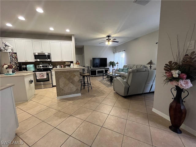 kitchen featuring appliances with stainless steel finishes, a kitchen island, white cabinetry, ceiling fan, and a breakfast bar