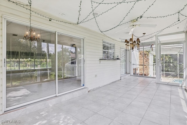 unfurnished sunroom featuring ceiling fan with notable chandelier