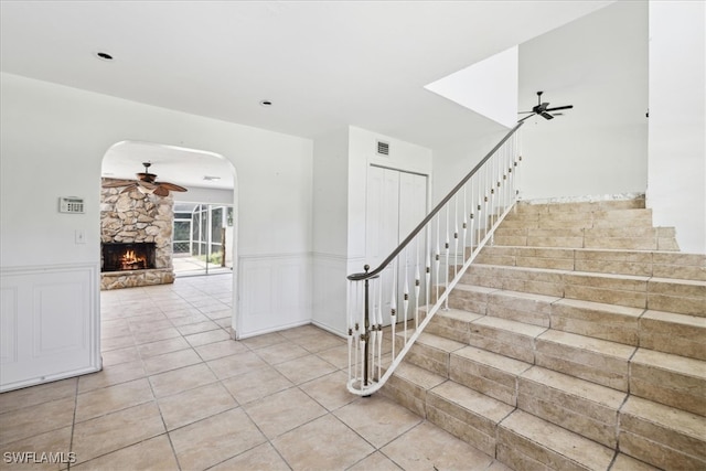 staircase featuring ceiling fan, a stone fireplace, and tile patterned floors