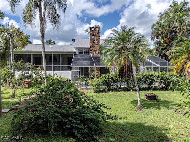 rear view of property with glass enclosure, a yard, and an outdoor fire pit