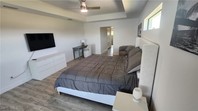 bedroom with hardwood / wood-style floors, ceiling fan, and a tray ceiling