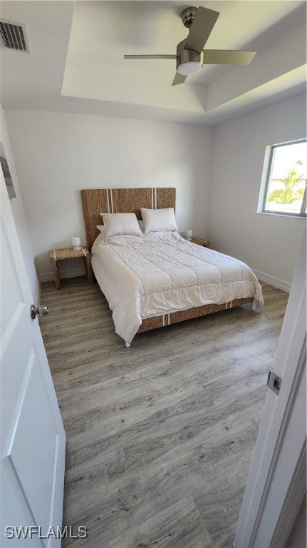 bedroom featuring hardwood / wood-style floors, ceiling fan, and a raised ceiling