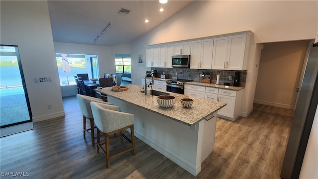 kitchen featuring a kitchen island with sink, high vaulted ceiling, light stone countertops, appliances with stainless steel finishes, and a breakfast bar area