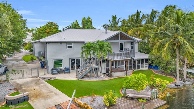 rear view of house featuring a yard, a sunroom, a patio, a deck with water view, and central AC unit