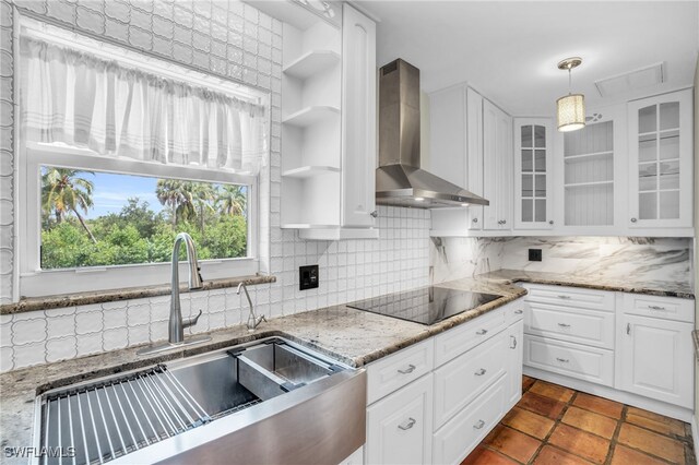 kitchen featuring white cabinets, backsplash, black electric cooktop, pendant lighting, and wall chimney exhaust hood