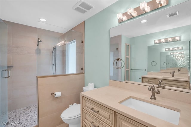 bathroom featuring vanity, a shower with shower door, toilet, and tile walls