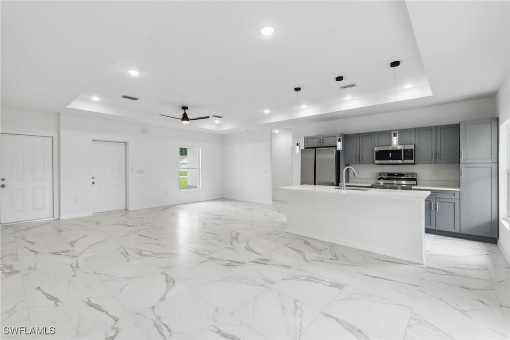 kitchen with appliances with stainless steel finishes, a center island with sink, a raised ceiling, and ceiling fan