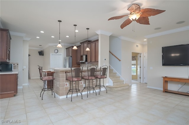 kitchen featuring pendant lighting, ornamental molding, stainless steel appliances, a kitchen breakfast bar, and ceiling fan