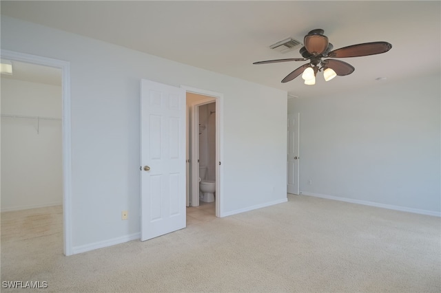 unfurnished bedroom with a spacious closet, a closet, light carpet, connected bathroom, and ceiling fan