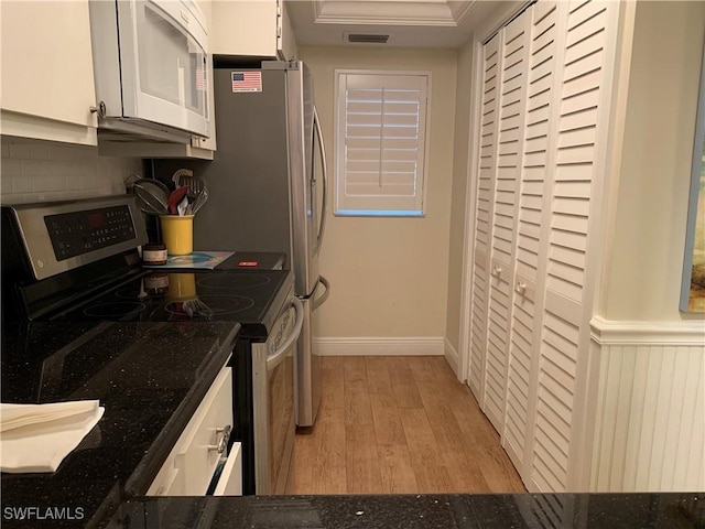 kitchen with white cabinets, light hardwood / wood-style floors, dark stone countertops, and stainless steel range oven