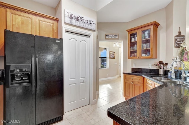 kitchen featuring dark stone counters, black fridge, light tile patterned flooring, and sink