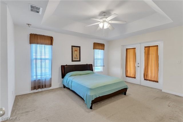 carpeted bedroom with french doors, multiple windows, ceiling fan, and a tray ceiling