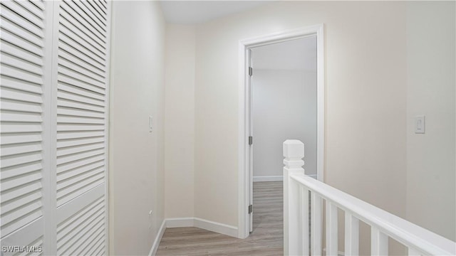 hallway featuring light wood-type flooring, baseboards, and an upstairs landing