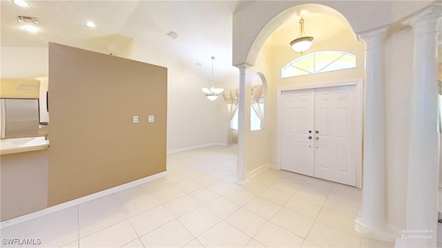 tiled entryway with a notable chandelier, high vaulted ceiling, and decorative columns