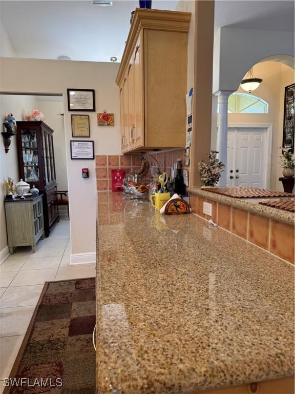 kitchen with backsplash, stone counters, ornate columns, light brown cabinetry, and light tile patterned flooring