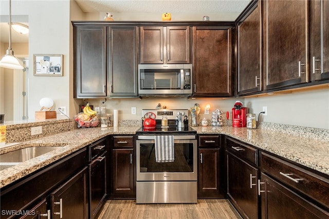 kitchen with light wood-type flooring, appliances with stainless steel finishes, light stone countertops, dark brown cabinetry, and a textured ceiling