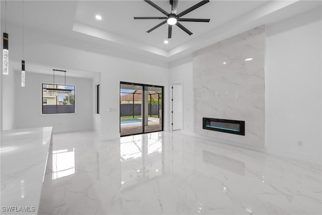 unfurnished living room featuring ceiling fan, a raised ceiling, and a fireplace