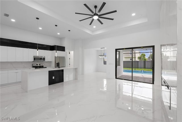 kitchen with a large island, appliances with stainless steel finishes, decorative light fixtures, and a tray ceiling