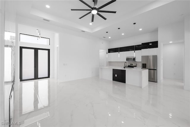 kitchen with appliances with stainless steel finishes, a tray ceiling, a center island with sink, and pendant lighting