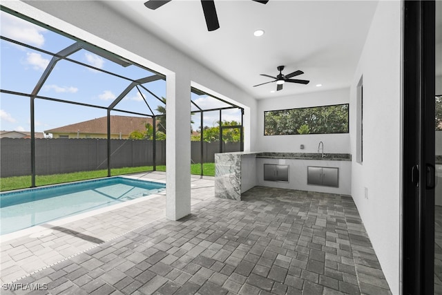 view of pool with a patio area, glass enclosure, sink, and ceiling fan