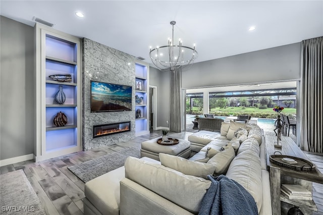 living room with an inviting chandelier, light hardwood / wood-style flooring, a fireplace, and built in features