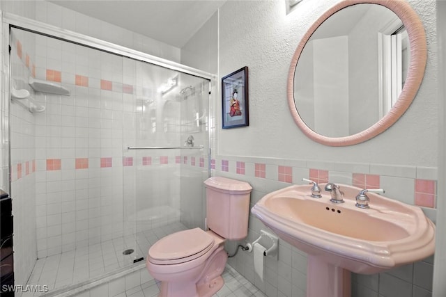 full bathroom featuring a wainscoted wall, toilet, a sink, tile walls, and a shower stall