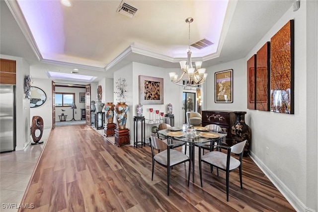 dining space with wood-type flooring, a raised ceiling, ornamental molding, and a notable chandelier