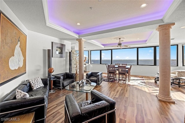 living area with wood finished floors, ornate columns, a tray ceiling, a textured ceiling, and crown molding