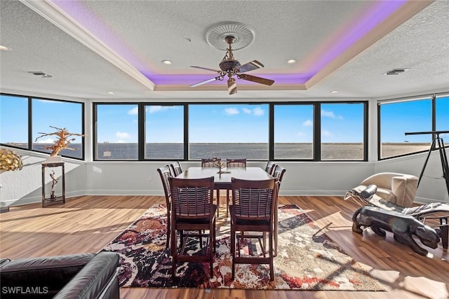 dining space featuring wood-type flooring, a textured ceiling, a water view, and a raised ceiling