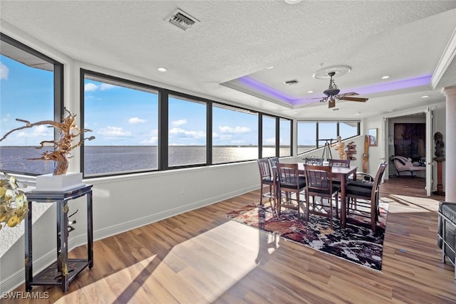 dining room with a raised ceiling, hardwood / wood-style floors, a water view, and a textured ceiling