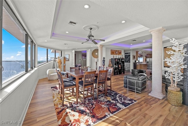 dining room featuring light wood-type flooring, ornate columns, a textured ceiling, a raised ceiling, and ceiling fan