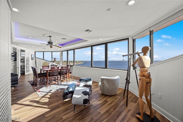 sunroom featuring a raised ceiling, visible vents, a water view, and ceiling fan