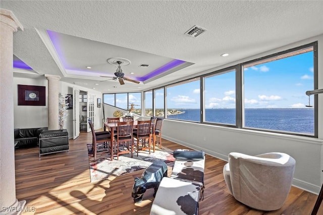 sunroom / solarium with a tray ceiling, ceiling fan, decorative columns, and a water view