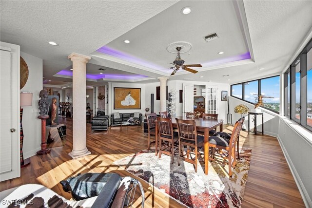 dining room featuring ornate columns, a textured ceiling, a raised ceiling, ceiling fan, and wood-type flooring