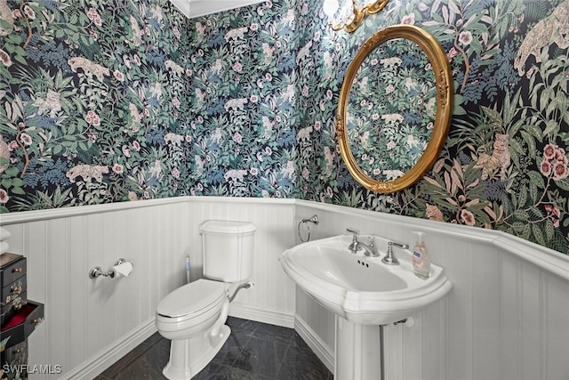 bathroom featuring wallpapered walls, toilet, a wainscoted wall, and a sink