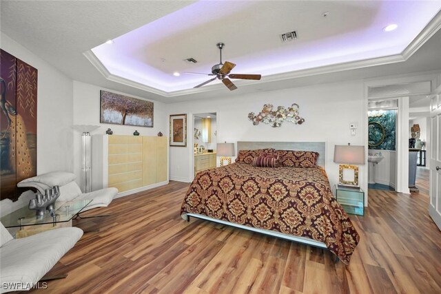 bedroom featuring a raised ceiling, connected bathroom, ceiling fan, and hardwood / wood-style flooring