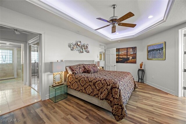 bedroom featuring hardwood / wood-style floors, ceiling fan, a raised ceiling, and connected bathroom